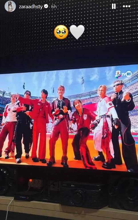 Layar televisi menampilkan penampilan grup musik di stadion besar saat acara Piala Dunia, dengan penonton memenuhi tribun.