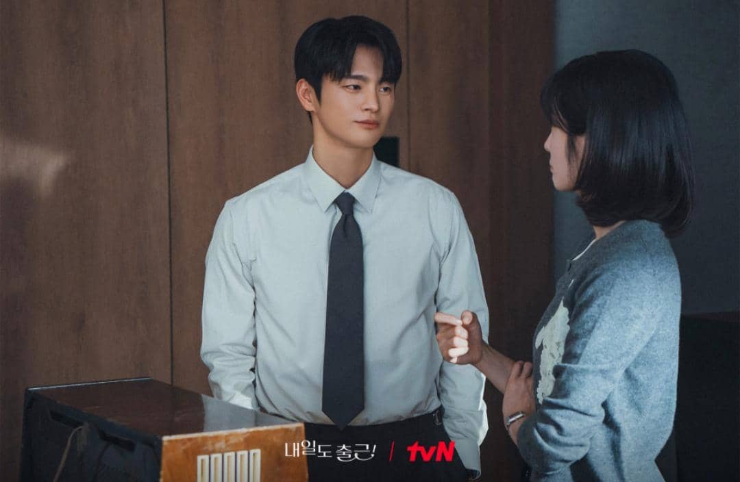 Dua karakter dalam drama See You at Work Tomorrow berdiri berhadapan di dalam ruangan dengan suasana serius.