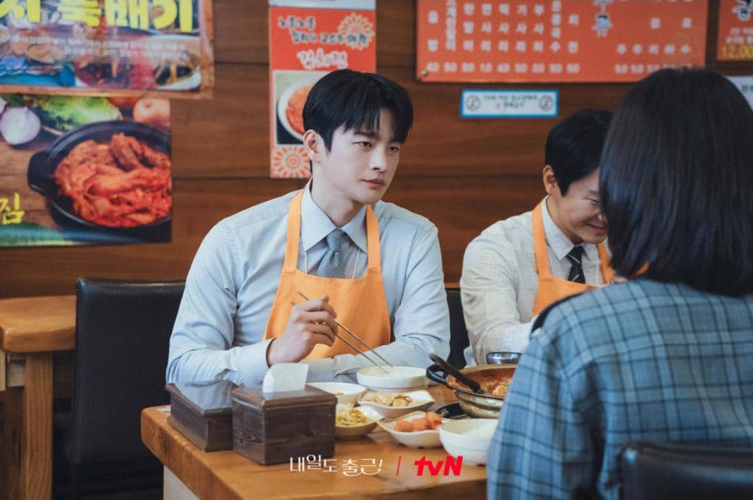 Adegan drama See You at Work Tomorrow menampilkan tiga orang sedang makan bersama di restoran Korea dengan suasana santai.