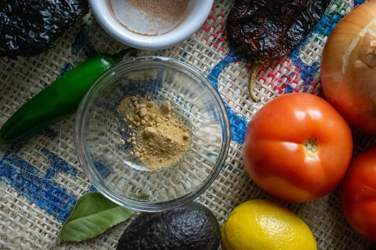 Bahan-bahan segar untuk membuat salsa termasuk tomat, cabai hijau, bawang, alpukat, lemon, dan rempah bubuk di atas kain goni.