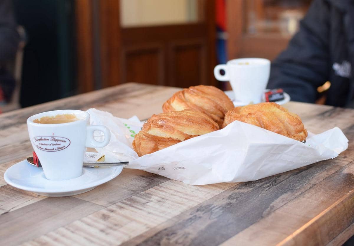 Segelas kopi dan roti di atas meja.