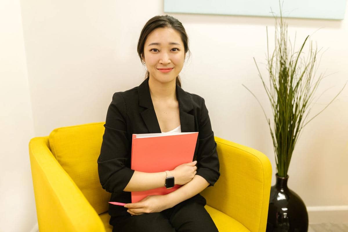 Ilustrasi seorang perempuan sedang bekerja di meja kerja dalam ruangan dengan perlengkapan kerja di sekitarnya.
