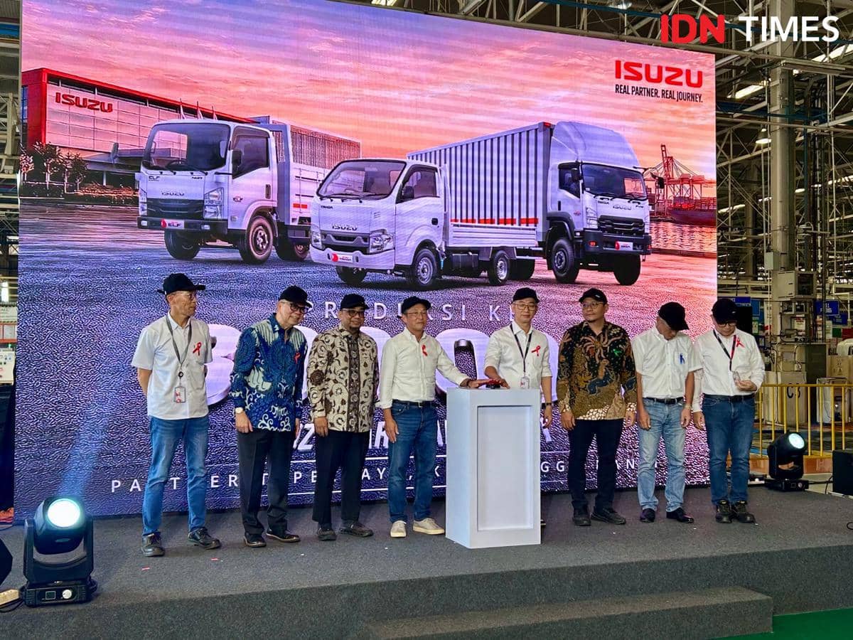 Sejumlah orang berdiri di atas panggung pabrik Isuzu Karawang dengan latar belakang truk dan gedung Isuzu berwarna merah.