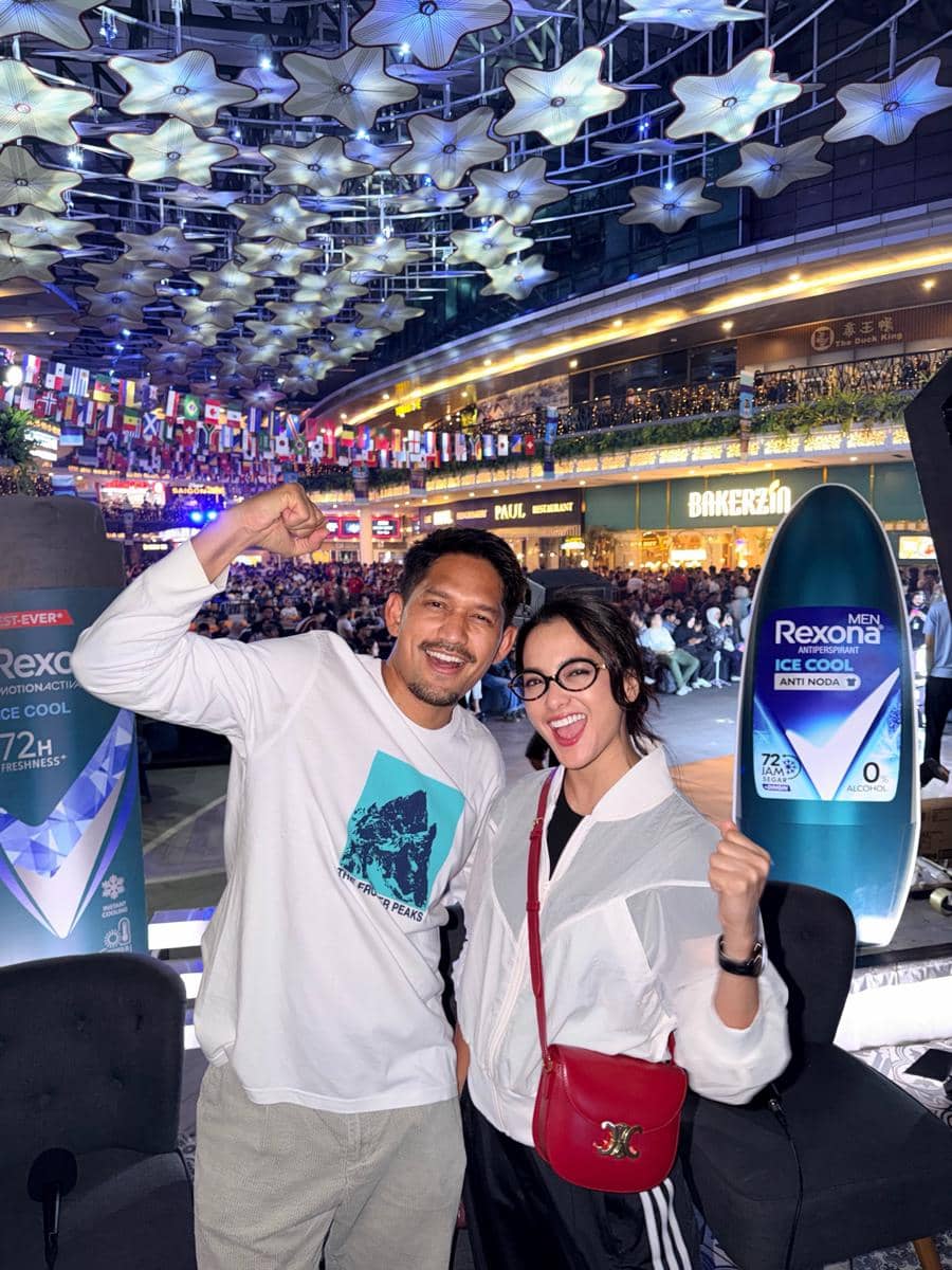 Dua orang berpose gembira di acara nonton bareng final Piala Dunia 2026 di pusat perbelanjaan dengan dekorasi bendera negara dan lampu berbentuk bintang.