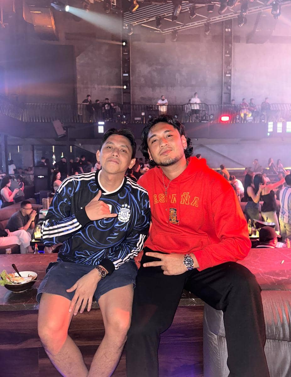 Dua pria berpose di tempat nobar final Piala Dunia 2026, satu mengenakan jaket tim Argentina dan satu memakai hoodie merah bertuliskan España.