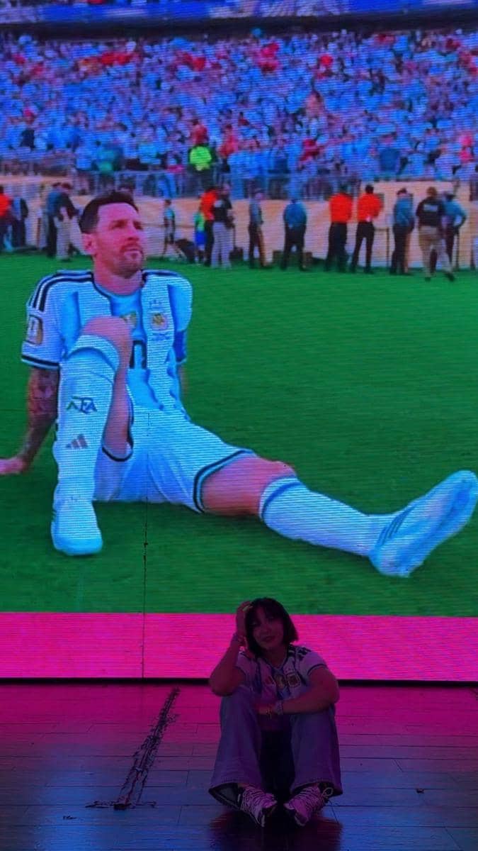 Seorang perempuan duduk di depan layar besar yang menampilkan pemain sepak bola Argentina di lapangan saat final Piala Dunia 2026.