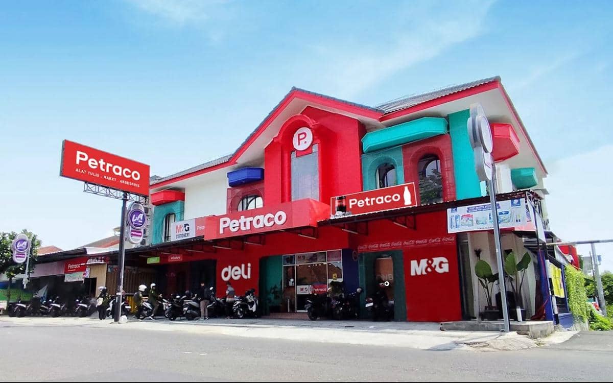 Bangunan toko alat tulis jogja Petraco berwarna merah dan putih dengan papan nama besar di bagian depan serta deretan motor di halamannya.