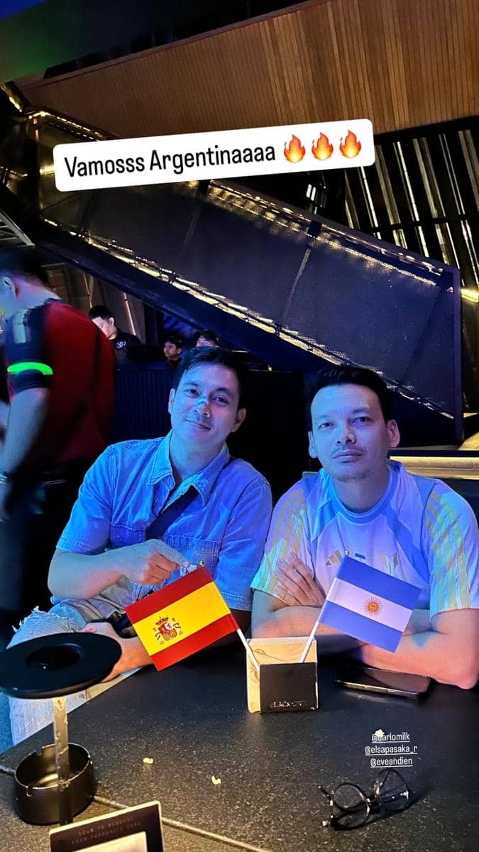 Dua pria duduk di meja dengan bendera Spanyol dan Argentina saat menonton bareng final Piala Dunia 2026 di tempat hiburan malam.