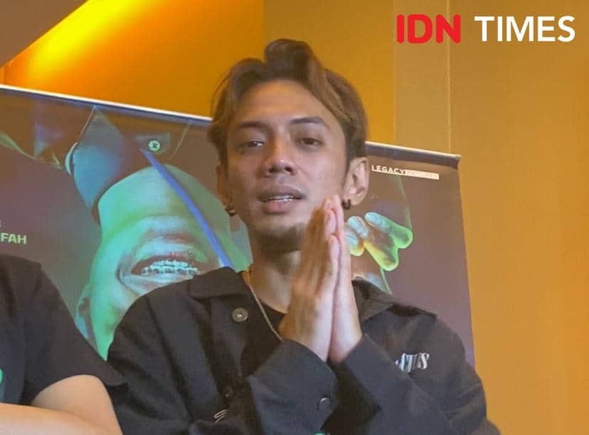 Seorang pria mengenakan jaket hitam berpose dengan tangan disatukan di depan poster film saat konferensi pers film Harusnya Horror di Jakarta.