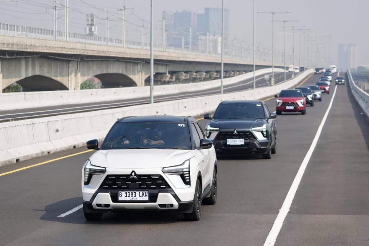 Beberapa unit Mitsubishi New Xforce HEV melaju beriringan di jalan tol dengan latar gedung perkotaan dan jembatan beton.