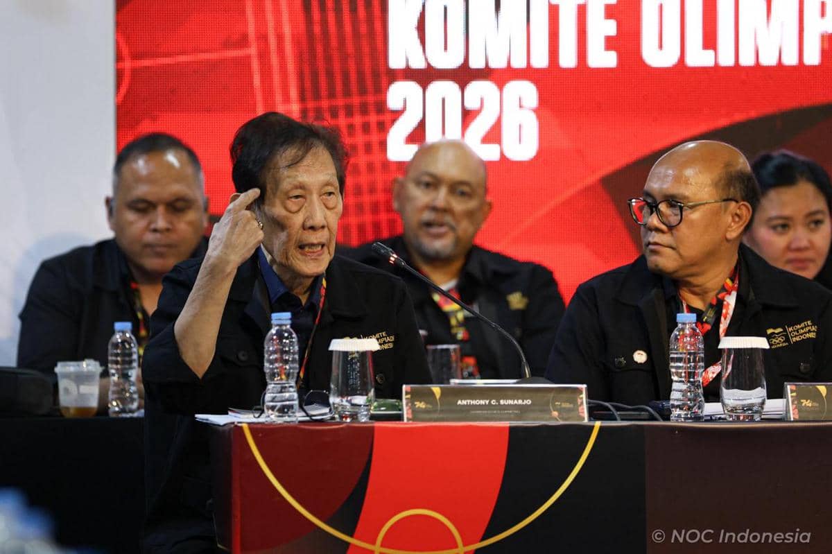 Beberapa anggota NOC Indonesia duduk di meja rapat mengenakan seragam hitam saat Rapat Anggota Luar Biasa dengan latar bertuliskan Komite Olimpiade 2026.