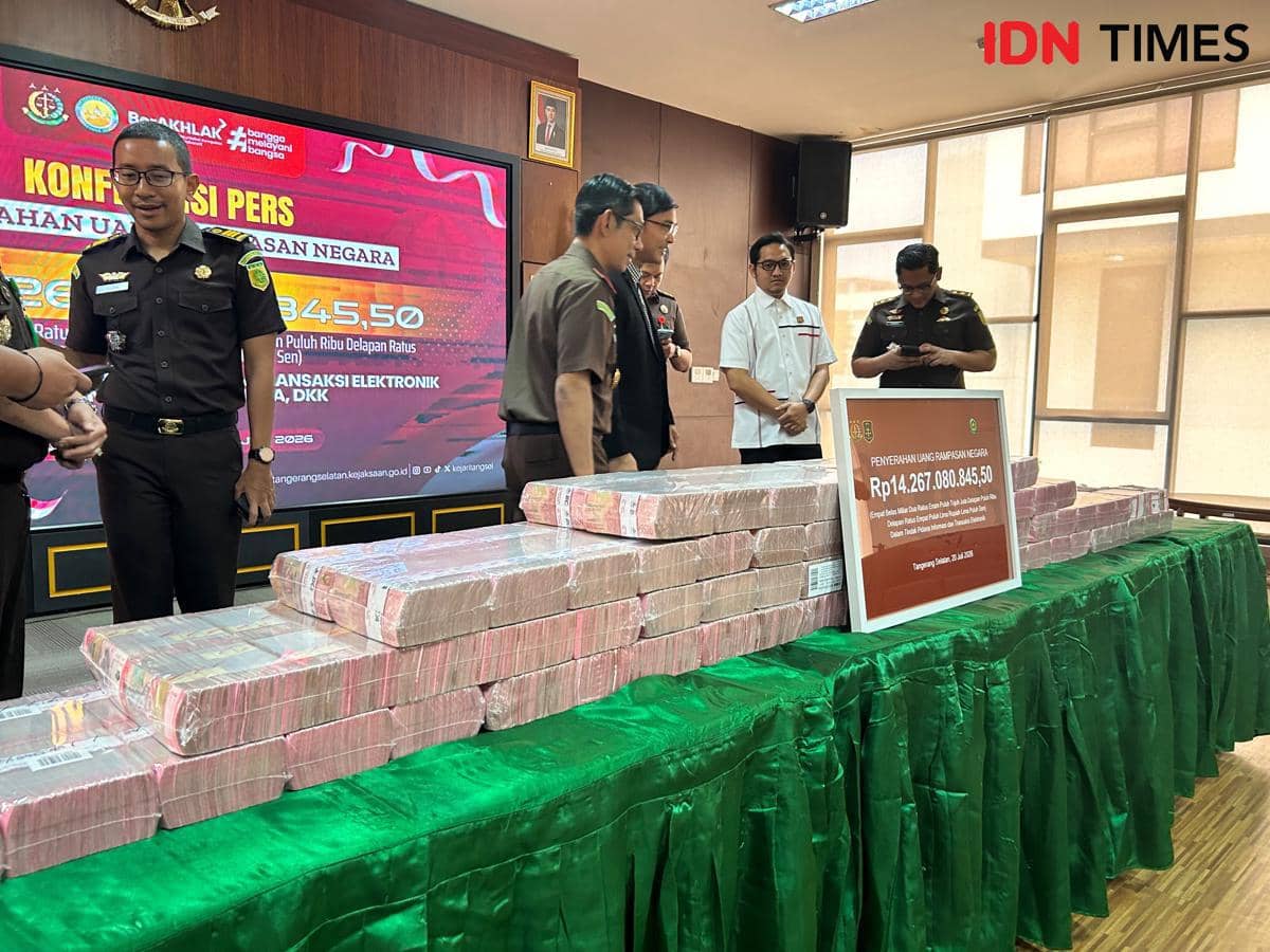 Petugas Kejaksaan Negeri Tangerang Selatan berdiri di dekat tumpukan uang tunai Rp14,2 miliar hasil kasus pinjaman online di ruang konferensi pers.