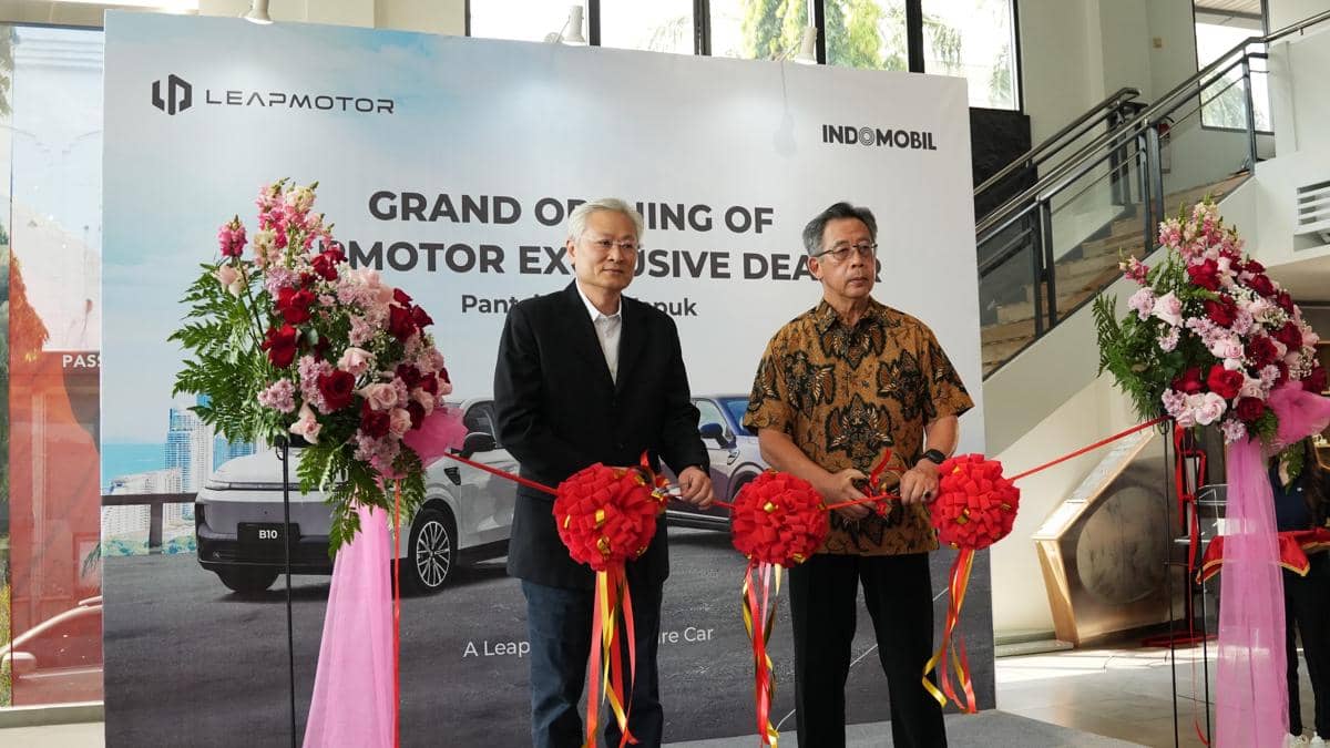 Dua pria memotong pita merah dalam seremoni peresmian diler baru Leapmotor yang bekerja sama dengan Indomobil di sebuah gedung.
