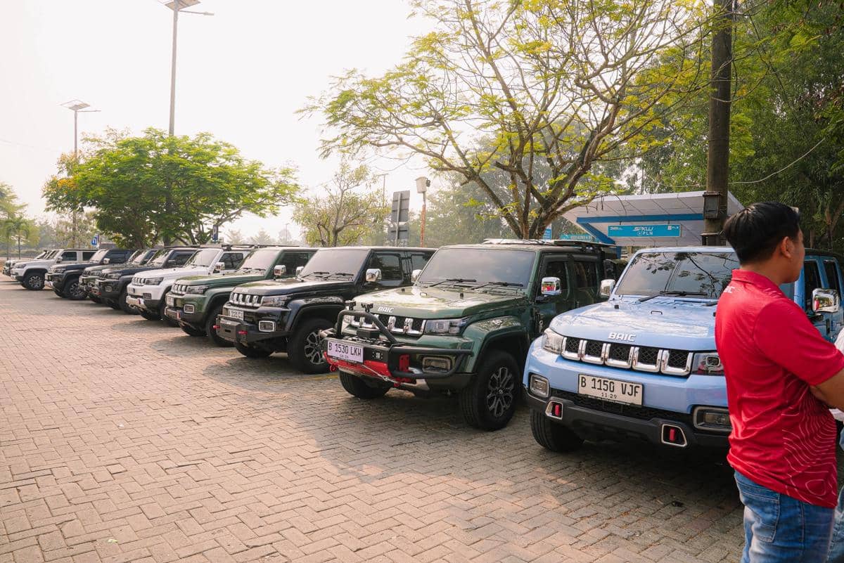 Deretan mobil SUV BAIC berbagai warna terparkir rapi di area terbuka dengan pepohonan rindang dan peserta mengenakan kaus merah.