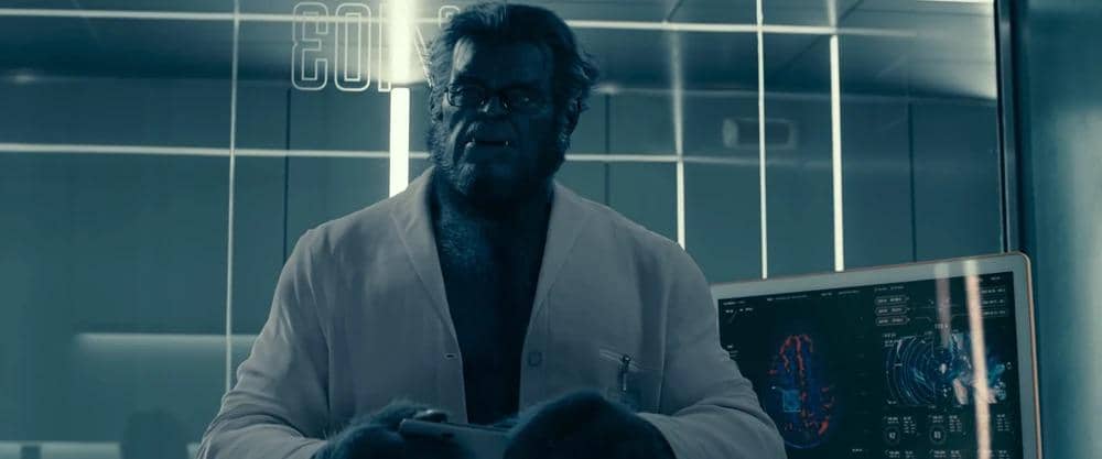 Karakter Beast berwujud makhluk berbulu biru mengenakan jas laboratorium putih di dalam ruangan ilmiah dengan layar komputer di belakangnya.