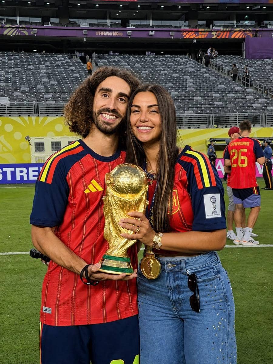 Sepasang pendukung tim nasional Spanyol mengenakan jersey merah memegang trofi Piala Dunia di stadion setelah kemenangan tim.