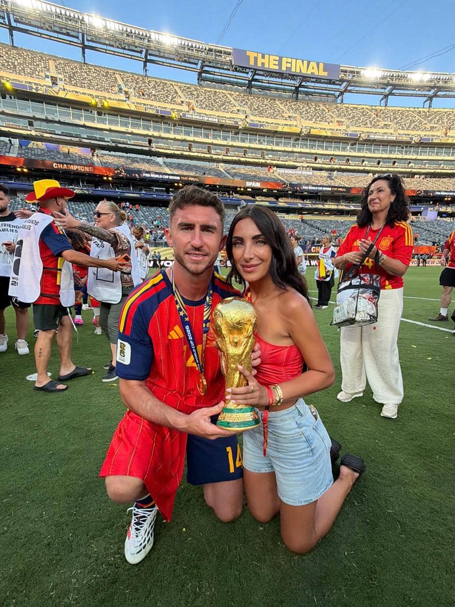 Seorang pemain timnas Spanyol berpose bersama pasangannya di lapangan sambil memegang trofi Piala Dunia 2026 setelah kemenangan.
