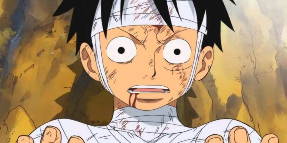 Karakter anime dengan tubuh penuh perban dan ekspresi terkejut berdiri di depan latar bebatuan setelah pertempuran sengit.