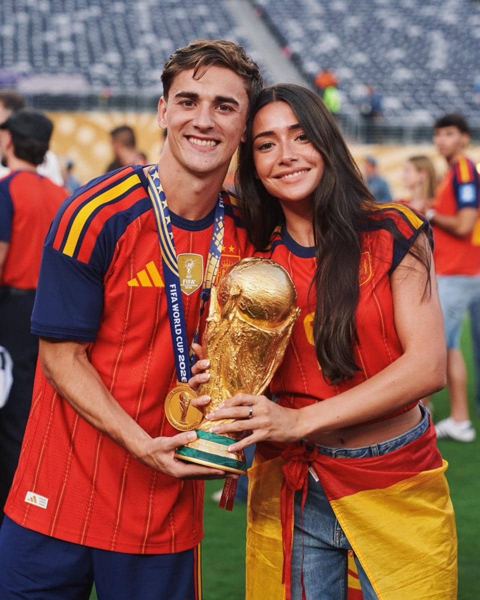 Seorang pemain tim nasional Spanyol berpose bersama pasangannya sambil memegang trofi Piala Dunia 2026 di stadion.