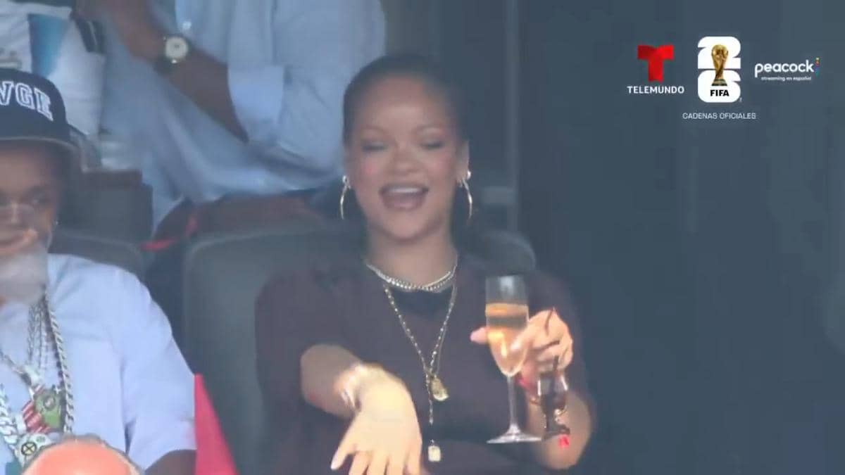 Seorang artis duduk di tribun VIP sambil memegang gelas minuman dan tersenyum saat menghadiri final Piala Dunia 2026.