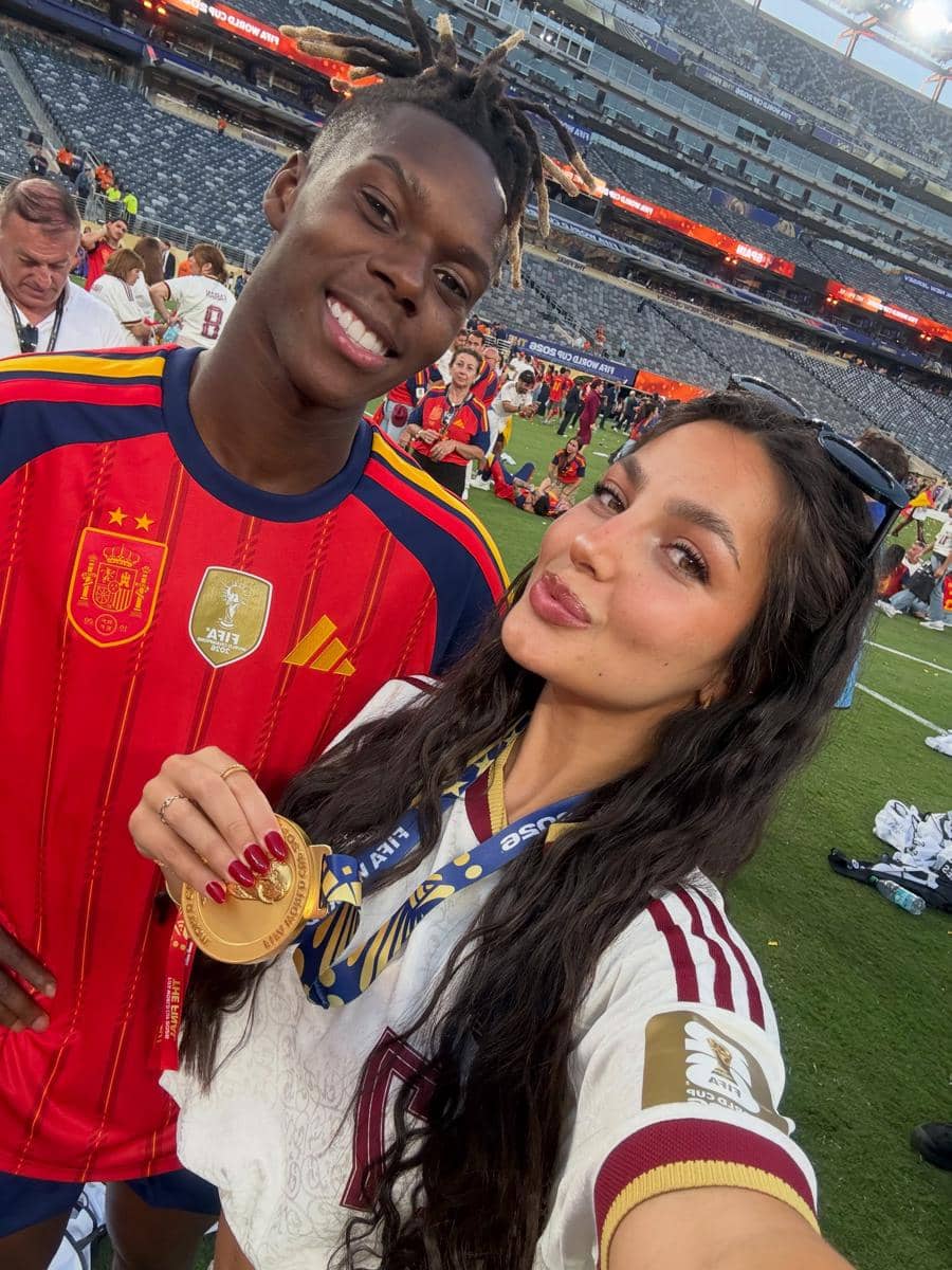 Seorang pemain tim nasional Spanyol berpose dengan seorang wanita yang memegang medali emas di stadion setelah kemenangan Piala Dunia 2026.