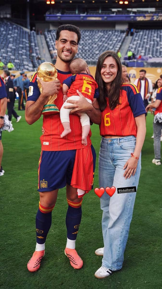 Seorang pemain tim nasional Spanyol memegang trofi Piala Dunia sambil berpose bersama pasangan dan bayi mereka di stadion setelah kemenangan.