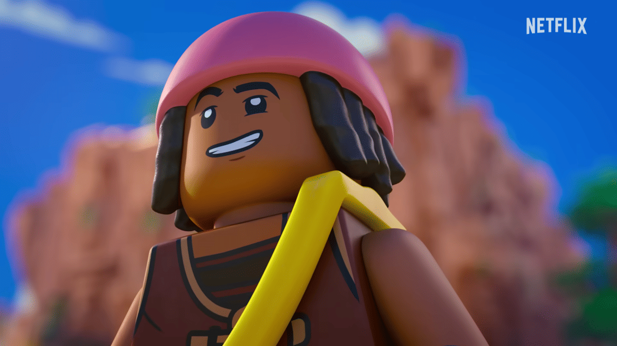 Karakter LEGO dengan helm merah muda dan rambut hitam tersenyum di bawah langit biru dengan latar tebing batu berwarna oranye.