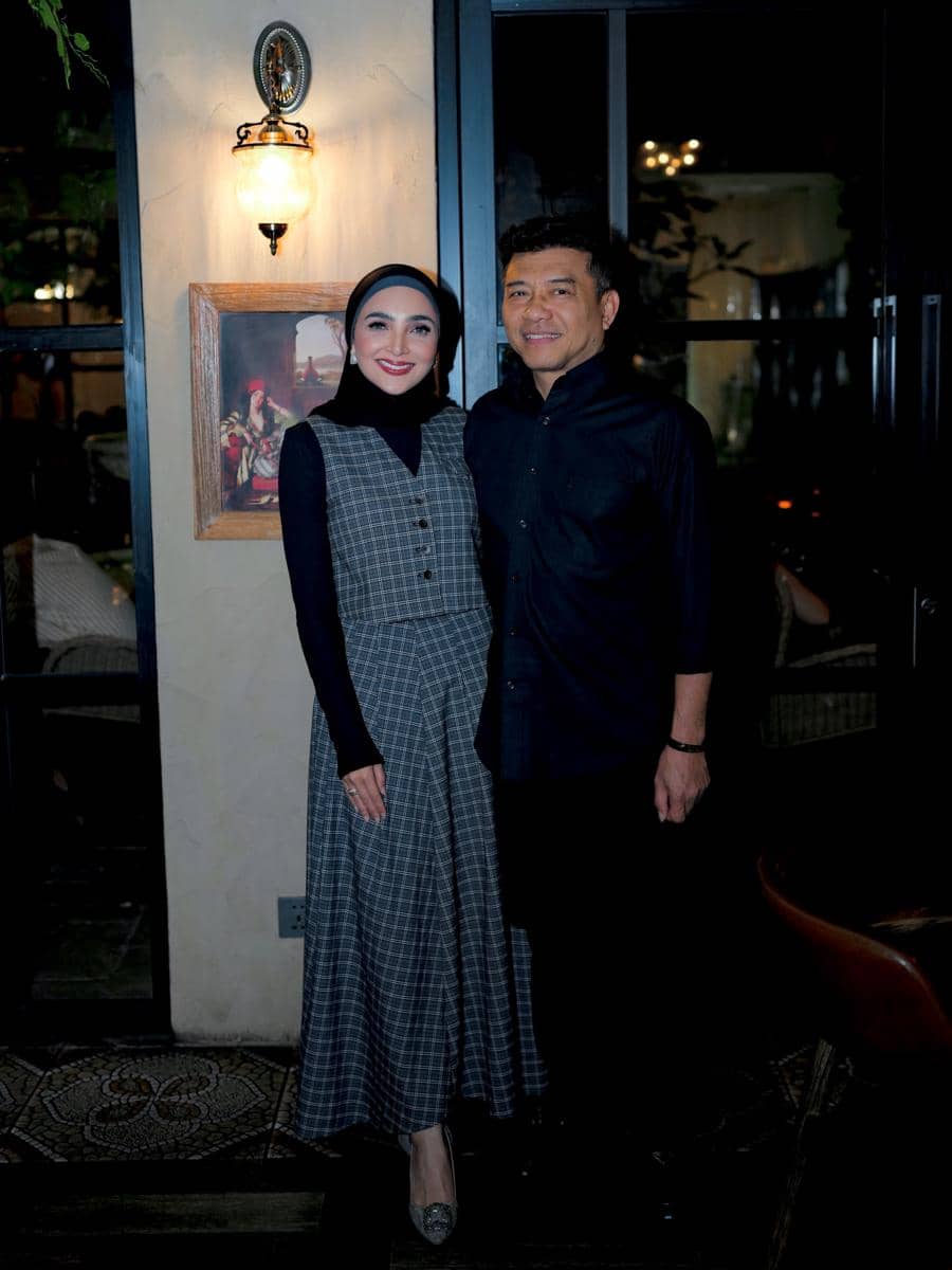 Seorang wanita berhijab berpose bersama seorang pria di dalam ruangan dengan pencahayaan hangat dan dekorasi dinding bergaya klasik.