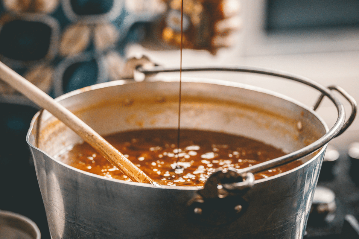 Panci logam berisi saus salsa taquera berwarna merah kecokelatan sedang diaduk dengan sendok kayu di dapur.