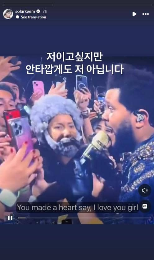Seorang penonton mengenakan kostum dan wig abu-abu di tengah kerumunan saat konser The Weeknd, sambil merekam dengan ponsel.