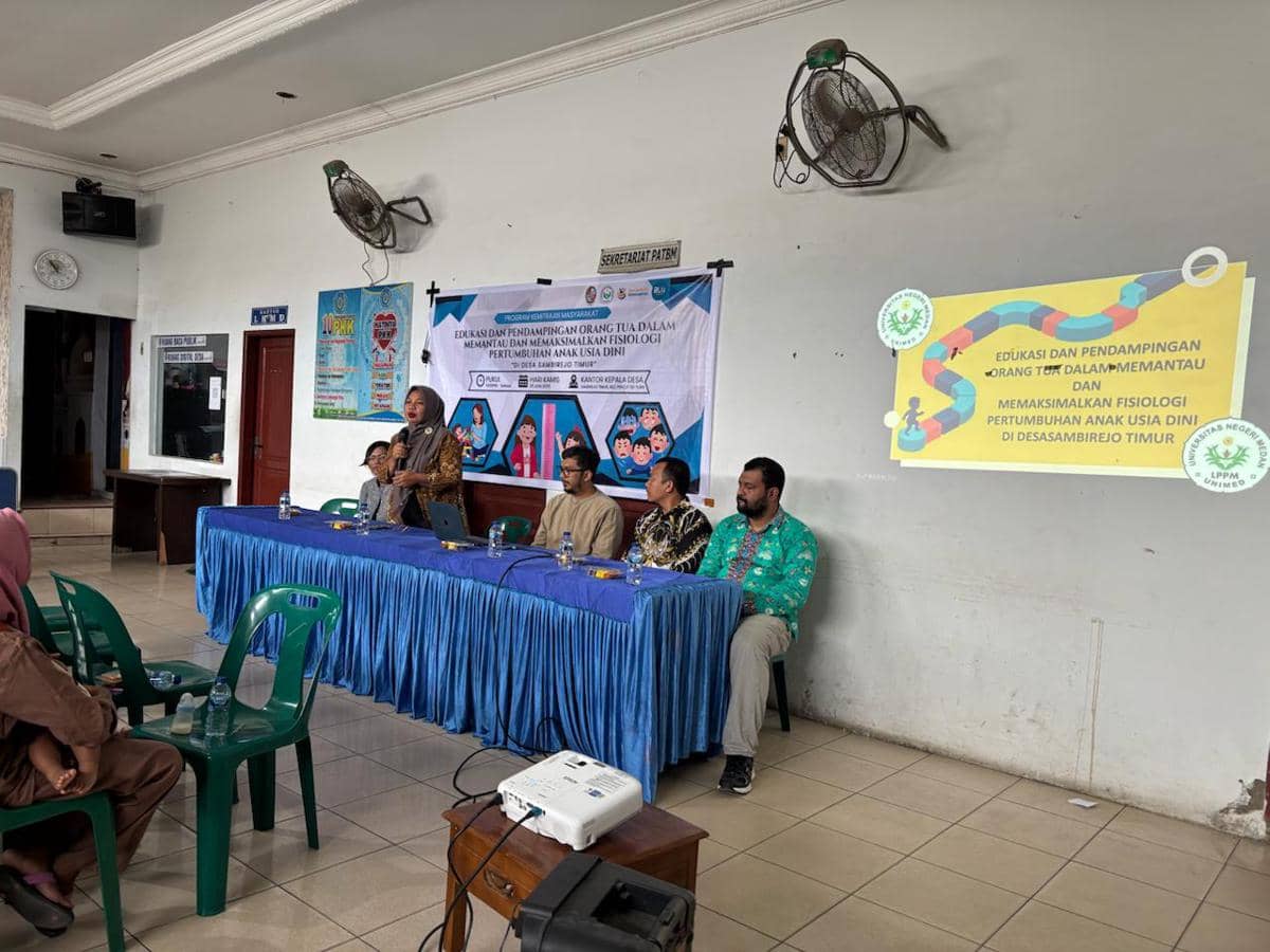 Kegiatan sosialisasi FIK Unimed di Desa Sambirejo Timur dengan beberapa narasumber duduk di meja depan dan peserta mendengarkan di aula desa.