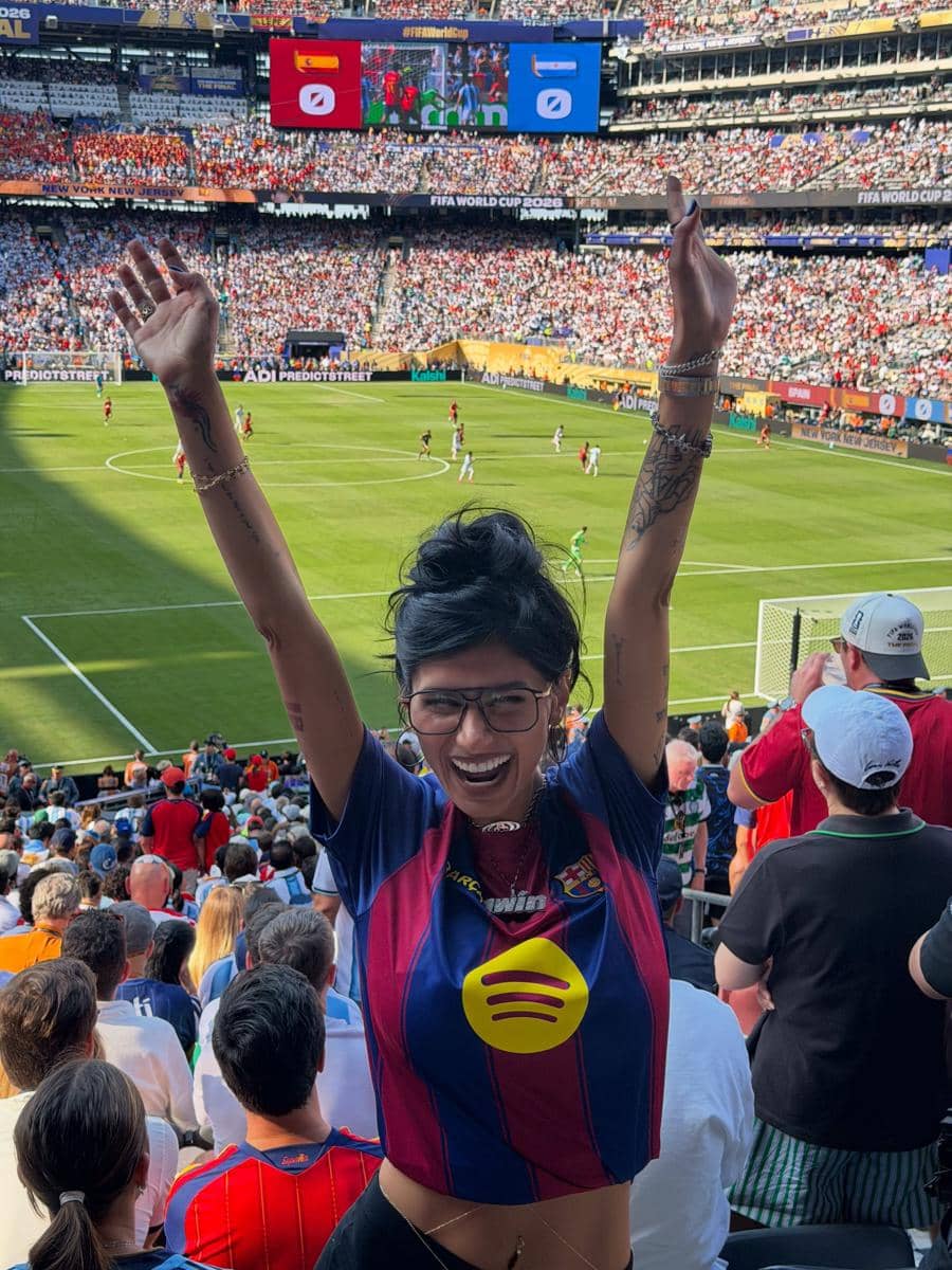 Seorang perempuan mengenakan jersey sepak bola mengangkat tangan dengan gembira di stadion yang penuh penonton saat final Piala Dunia 2026.