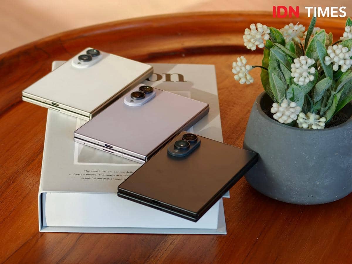 Tiga unit Samsung Galaxy Z Fold8 berwarna putih, ungu, dan hitam terlipat rapi di atas buku di meja kayu dengan pot tanaman hias di sampingnya.