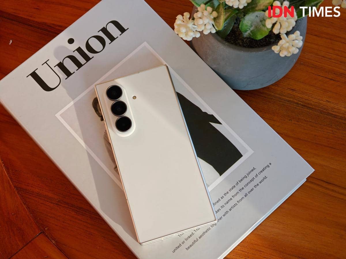 Samsung Galaxy Z Fold8 Ultra berwarna putih dengan tiga kamera belakang diletakkan di atas majalah Union di meja kayu dengan pot tanaman kecil di sampingnya.