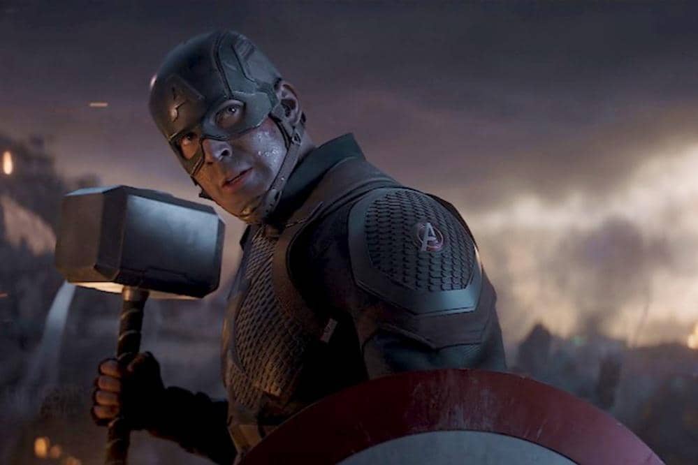 Captain America mengenakan kostum tempur sambil memegang palu Mjölnir dan perisai di medan pertempuran dalam film Avengers: Endgame.