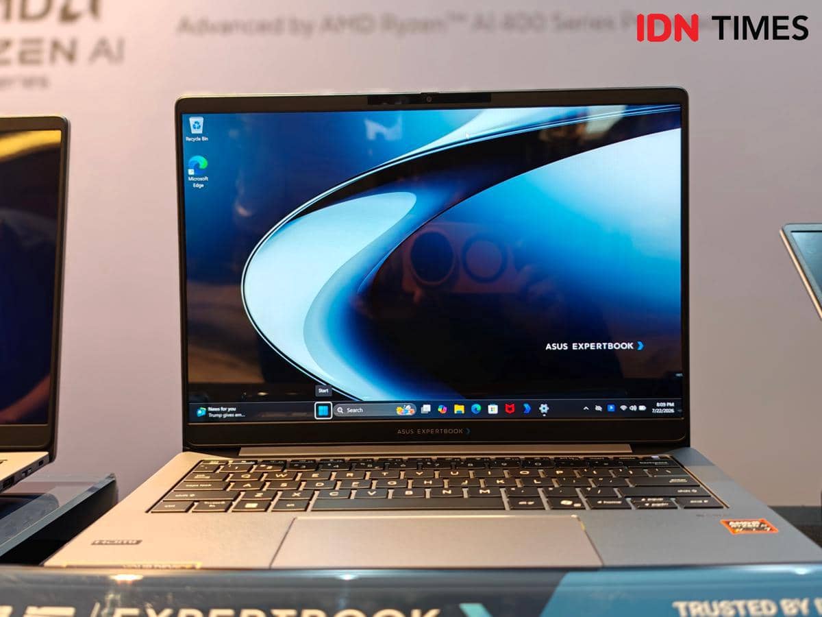 Laptop ASUS ExpertBook P5 G2 dengan layar menyala menampilkan antarmuka Windows, dipamerkan di atas meja dengan latar promosi prosesor AMD Ryzen AI.
