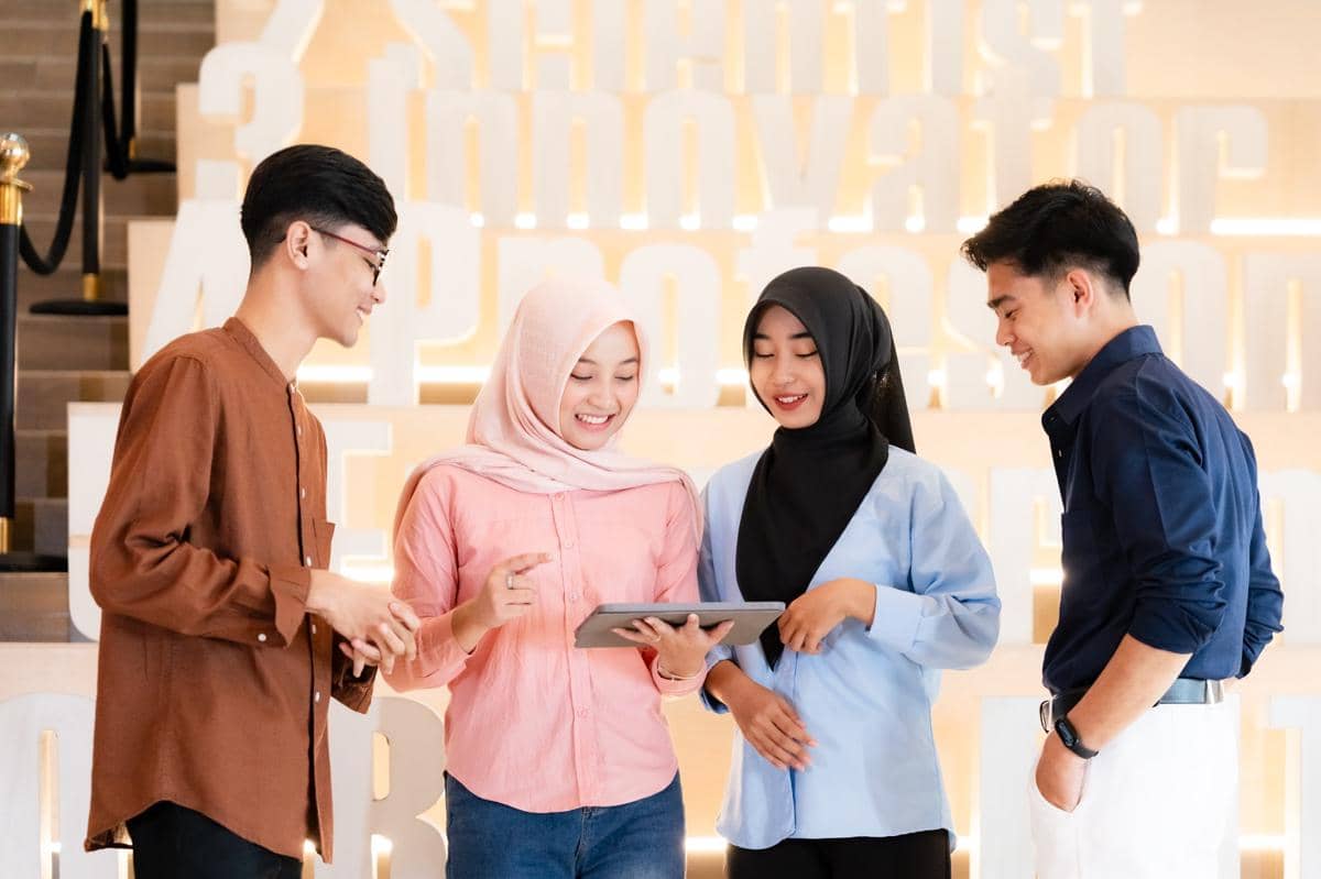 Empat mahasiswa Universitas Nahdlatul Ulama Yogyakarta berdiskusi sambil melihat tablet di area kampus dengan suasana cerah dan modern.