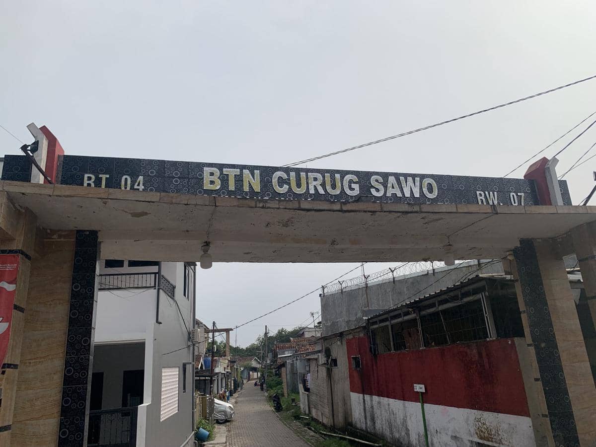 Gerbang masuk perumahan BTN Curug Sawo RT 04 RW 07 dengan jalan kecil di antara deretan rumah di kawasan pemukiman.