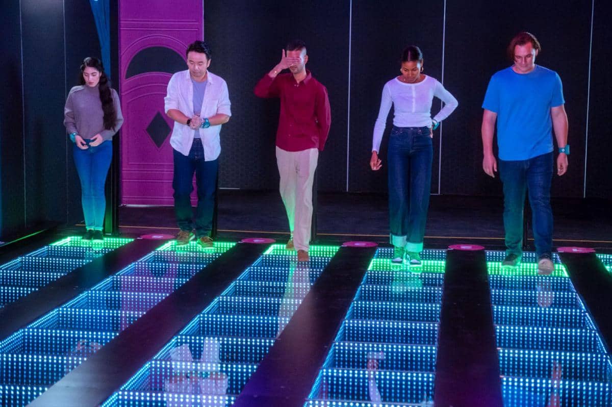 Lima orang peserta berjalan di atas lantai kaca bercahaya warna-warni dalam arena permainan interaktif Squid Game: The Experience.