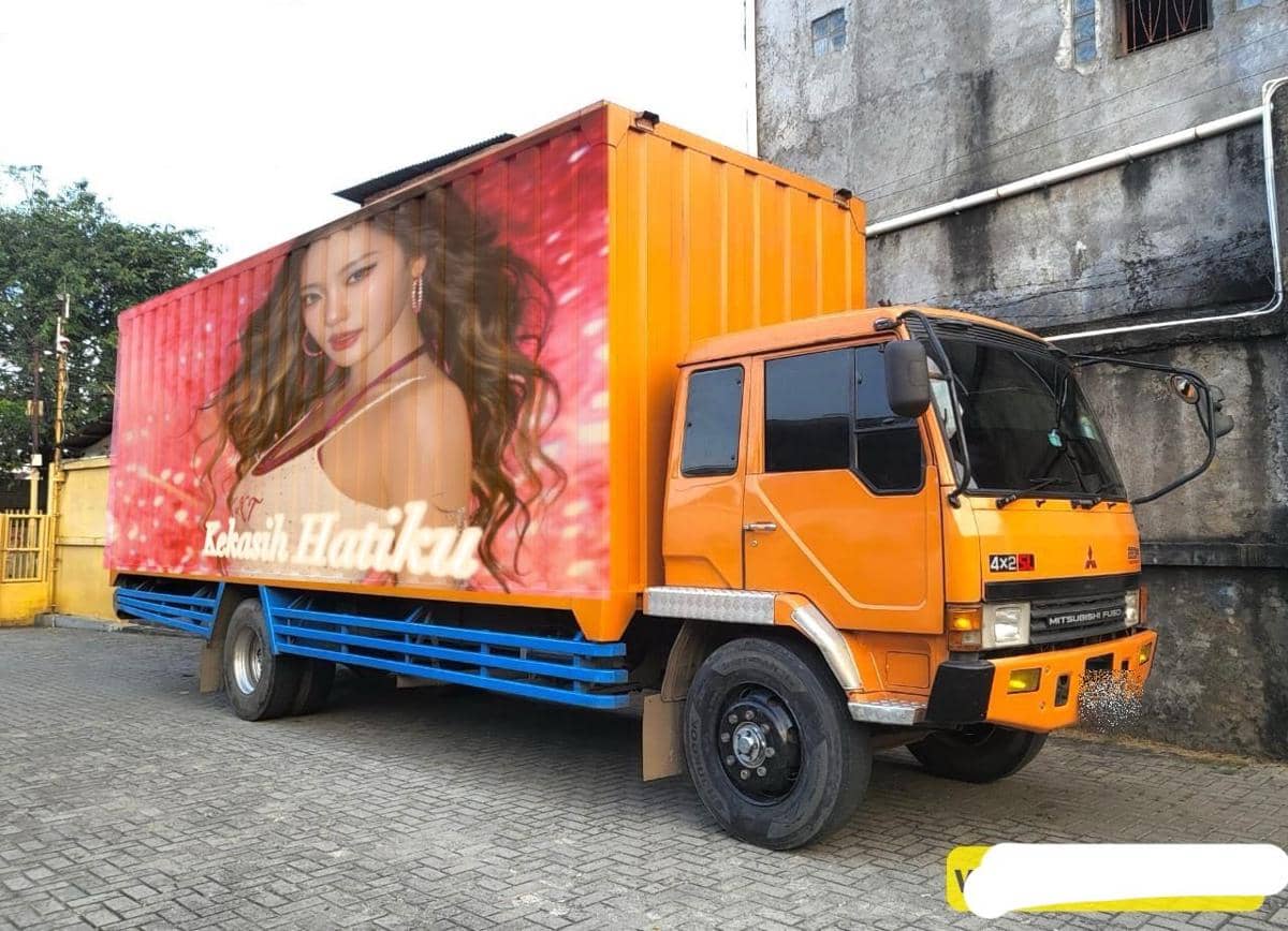 Truk berwarna oranye dengan gambar wanita berambut panjang di sisi bak bertuliskan 'Kekasih Hatiku' berlatar merah muda.