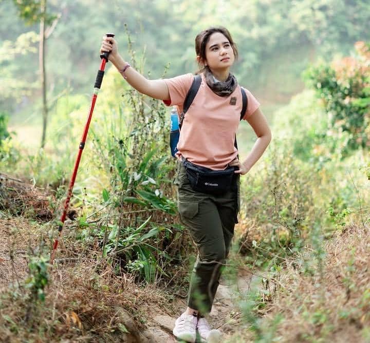 Tissa Biani berpose saat trekking di jalur menuju Curug Sentul dengan latar pepohonan hijau yang rimbun.