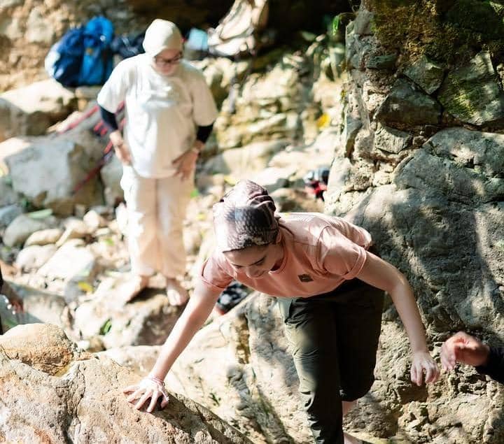 Tissa Biani berpose di jalur trekking Curug Sentul dengan latar pepohonan hijau rindang dan bebatuan alam.