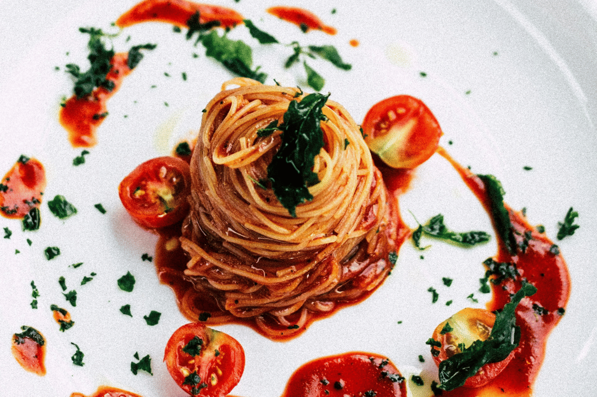 Semangkuk pasta tomat pedas berwarna merah dengan taburan bumbu dan daun hijau, disajikan sebagai ilustrasi makanan.