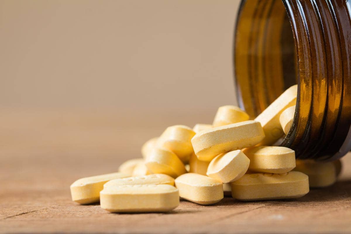 Ilustrasi pil vitamin C berwarna putih dan kuning yang tersusun di atas permukaan biru muda yang bersih.