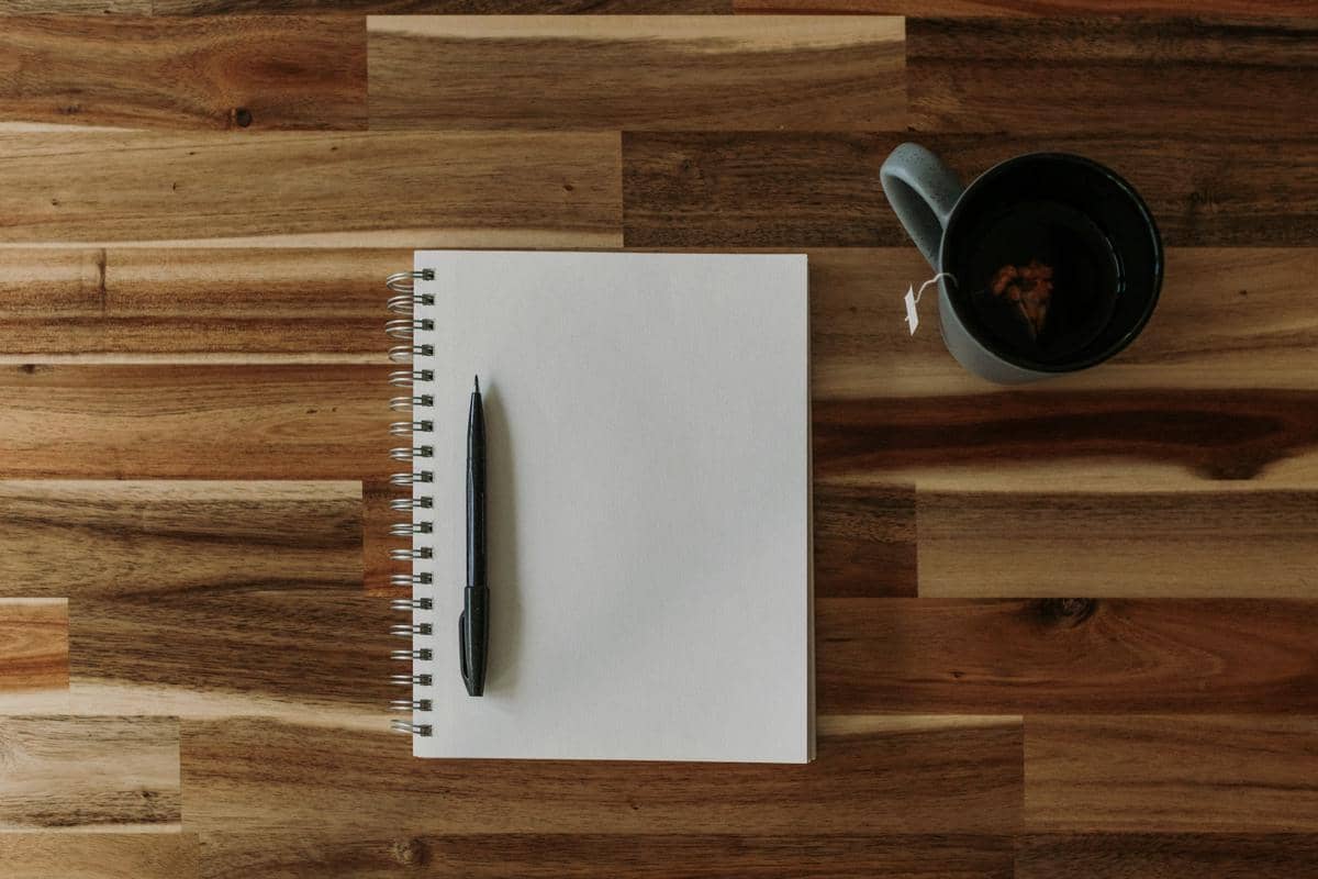 Notebook kertas terbuka dengan halaman kosong di atas meja, sebagai ilustrasi kegiatan mencatat dan menulis.