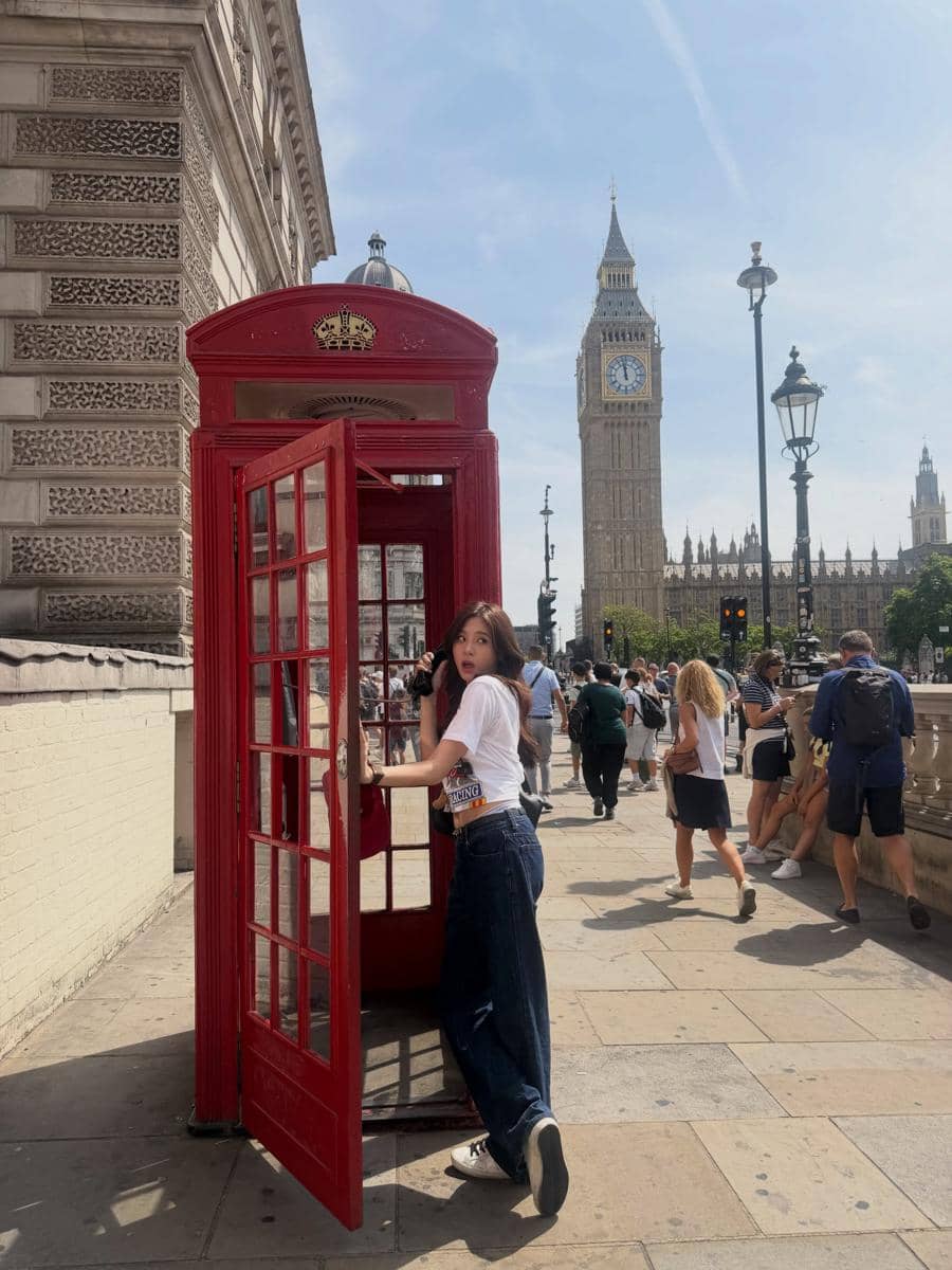 Azizi Asadel berjalan-jalan di sekitar Big Ben, London, dengan latar menara jam ikonik di bawah langit cerah.