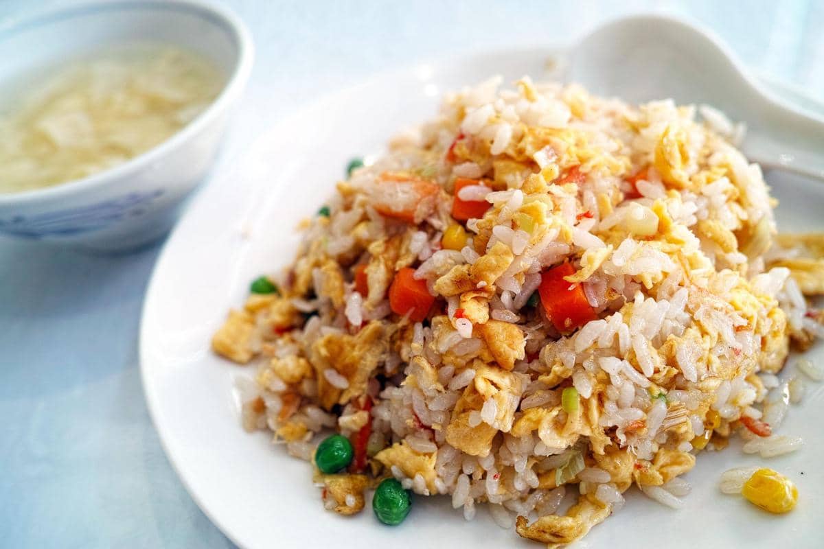 Seporsi nasi goreng Yangzhou berwarna keemasan disajikan dalam mangkuk putih dengan campuran sayuran dan telur.