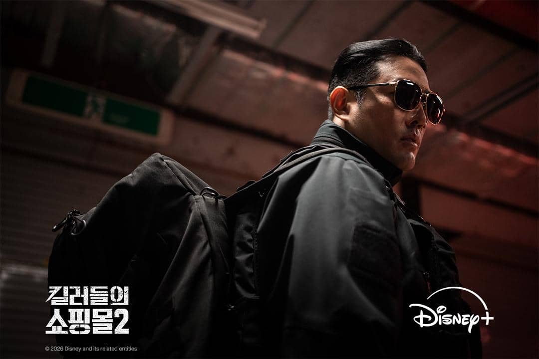 Jo Han Sun tampil mengenakan setelan gelap dengan ekspresi serius dalam drama Korea A Shop for Killers musim kedua.