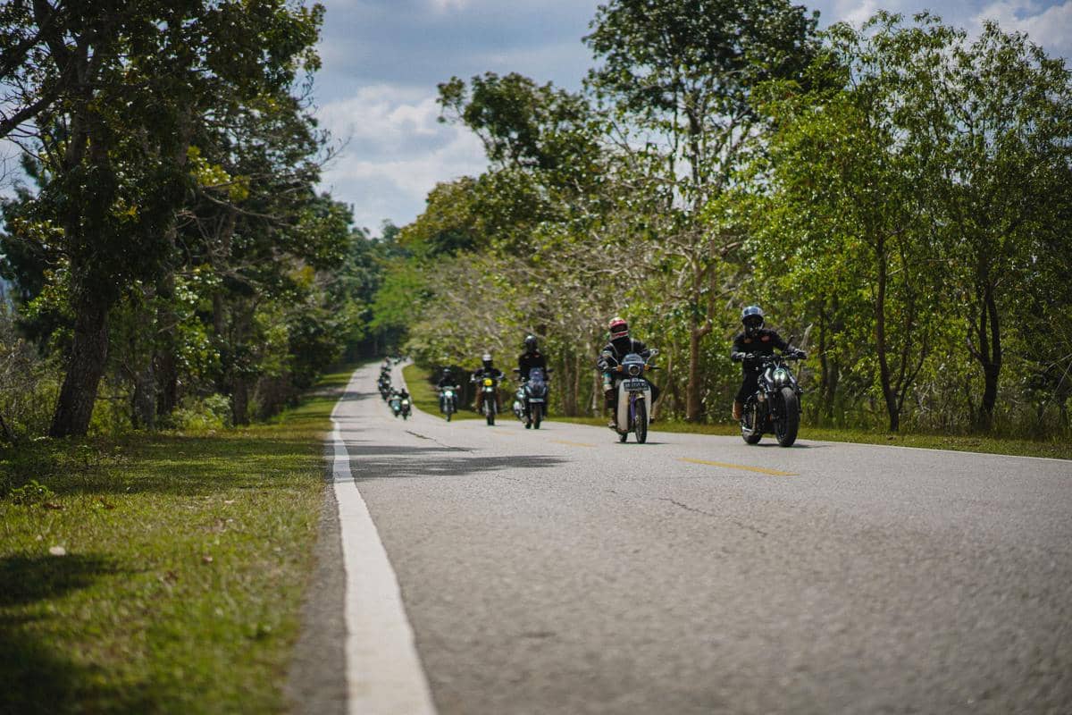Seorang pengendara sepeda motor melintasi jalan di Sumba dalam perjalanan touring, dengan lanskap pulau di sekelilingnya.