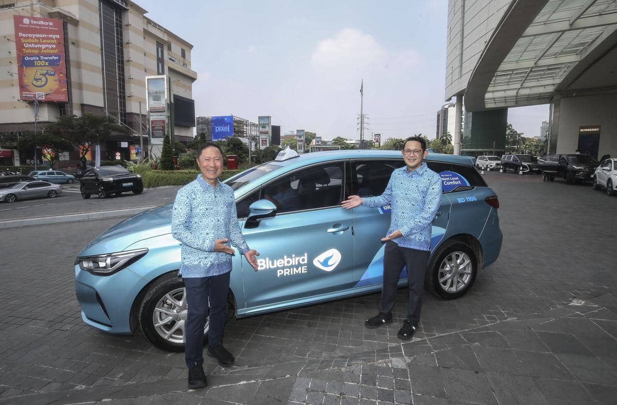 Sigit dan Andre Djokosoetono berada di depan armada Bluebird Prime, dengan latar sejumlah kendaraan transportasi.